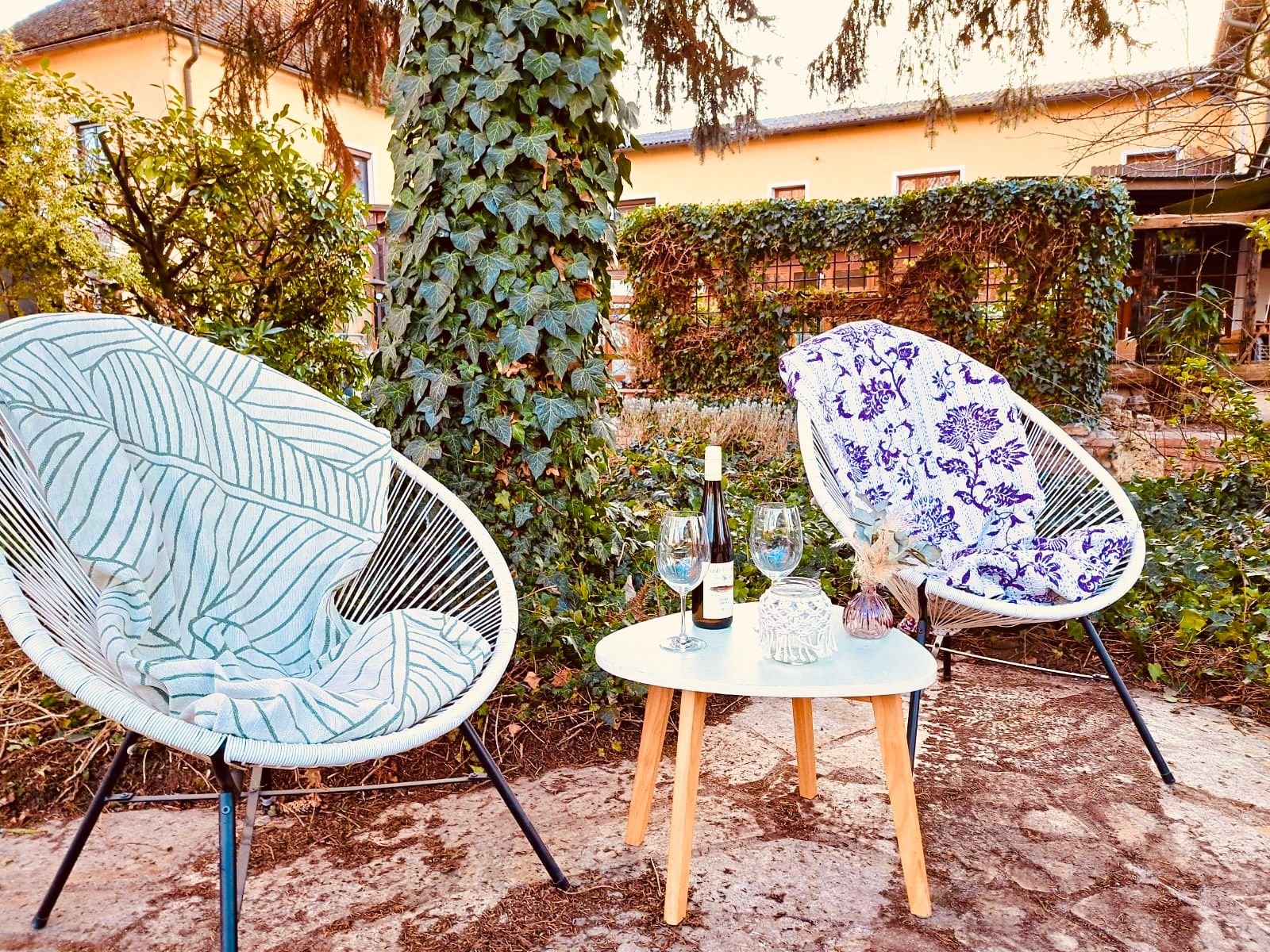 Zwei Stühle mit Decken und ein Tisch mit Wein und Gläsern in einem Garten.