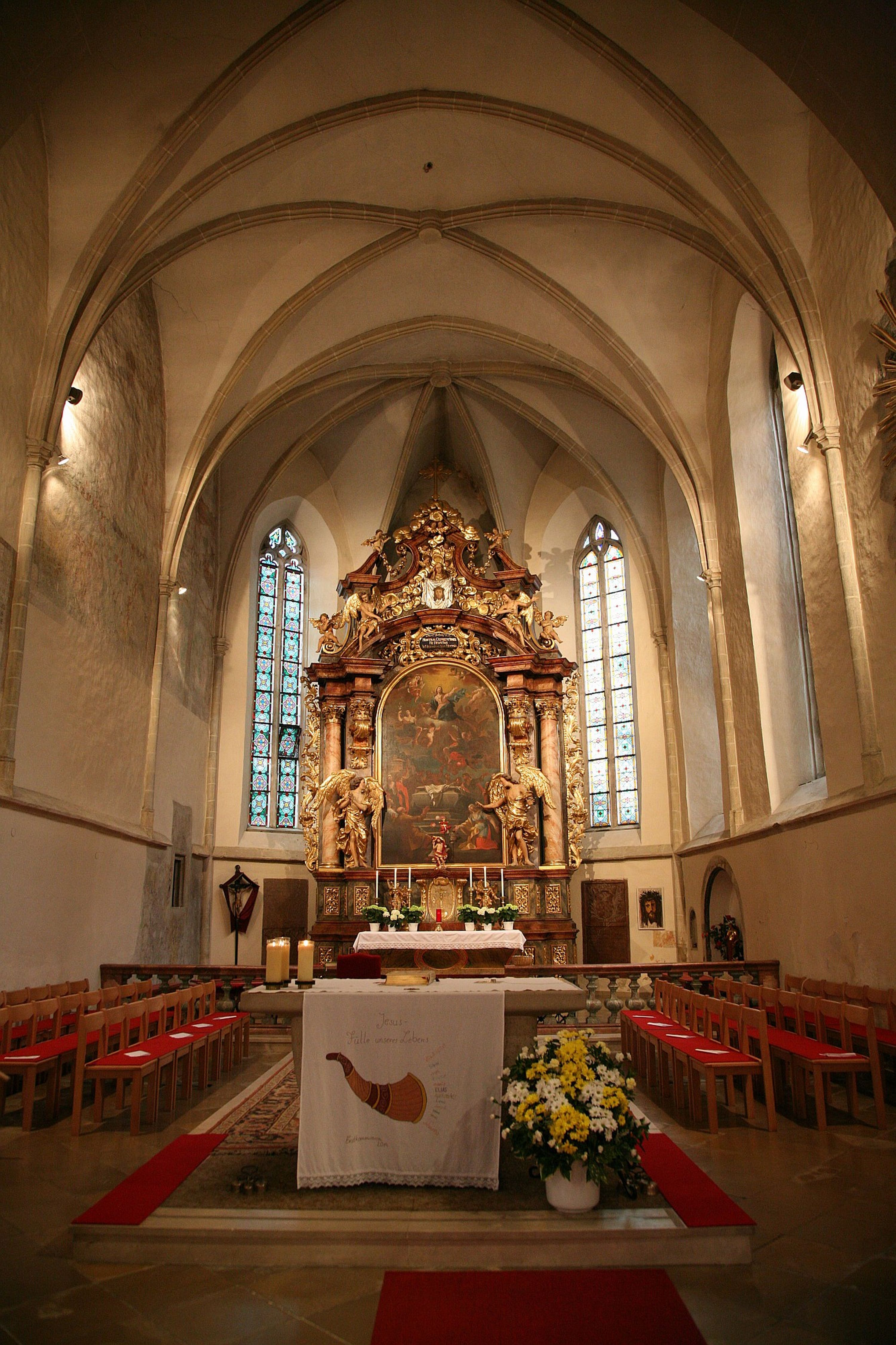 Innenansicht einer Kirche mit Altar und Buntglasfenstern.