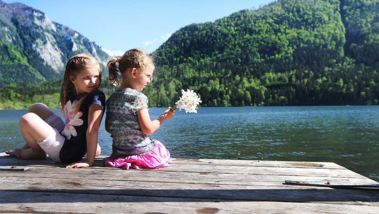 Zwei Kinder sitzen auf einem Steg am Lunzer See mit Bergen im Hintergrund.