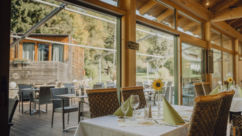 A restaurant with a winter garden and terrace, tables set with sunflowers and a view of the green surroundings.